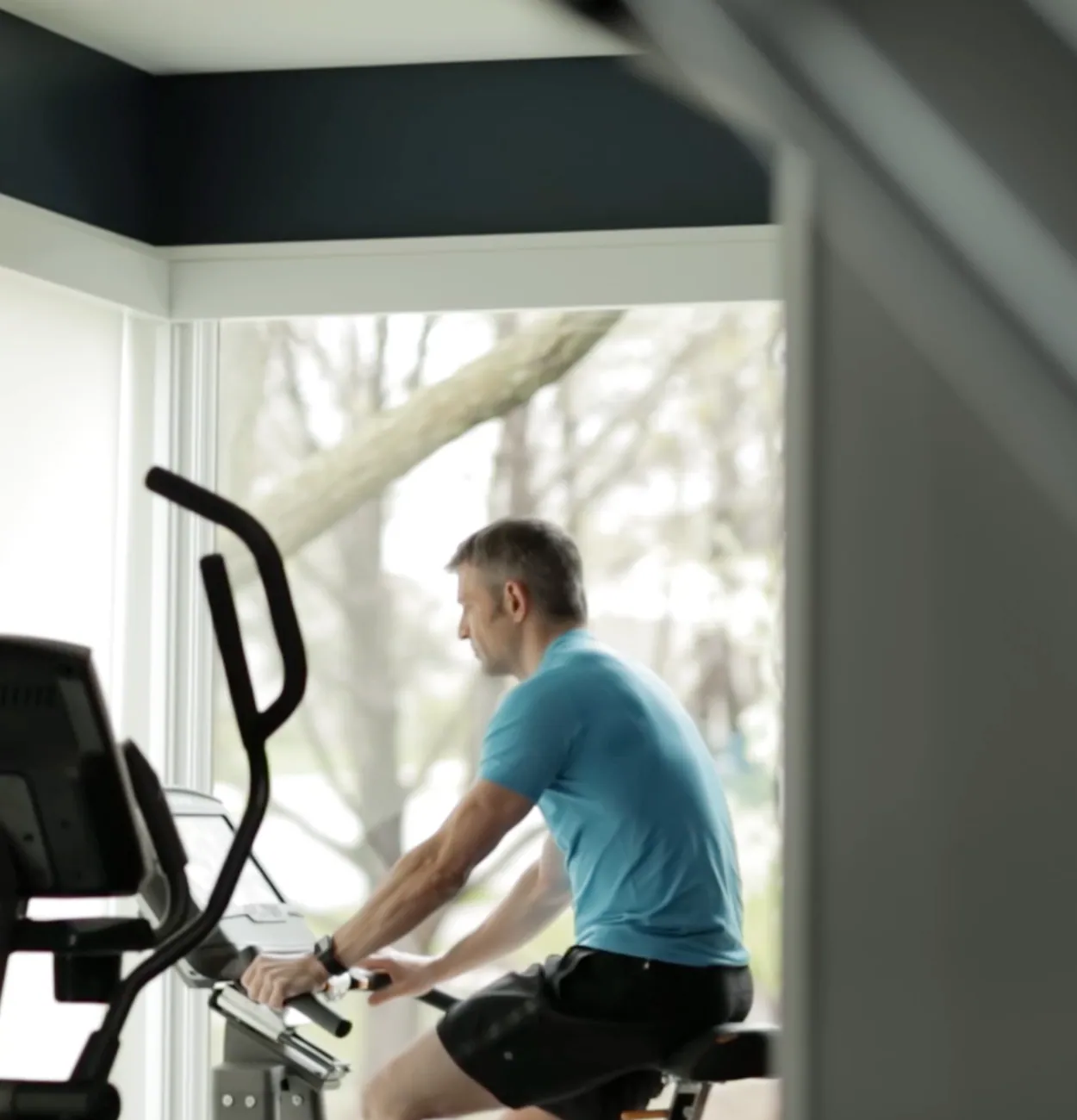 A middle aged man riding a stationery bike in front of a window.